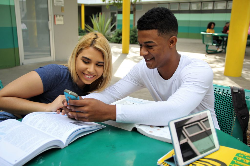 Foto de dos estudiantes utilizando el celular para ver cursos en linea. 